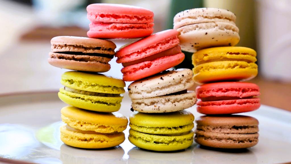 A vibrant stack of vegan macarons in flavors like salted caramel, pistachio, strawberry-rose, and cassis. Gluten-free, dairy-free, and available for nationwide delivery.