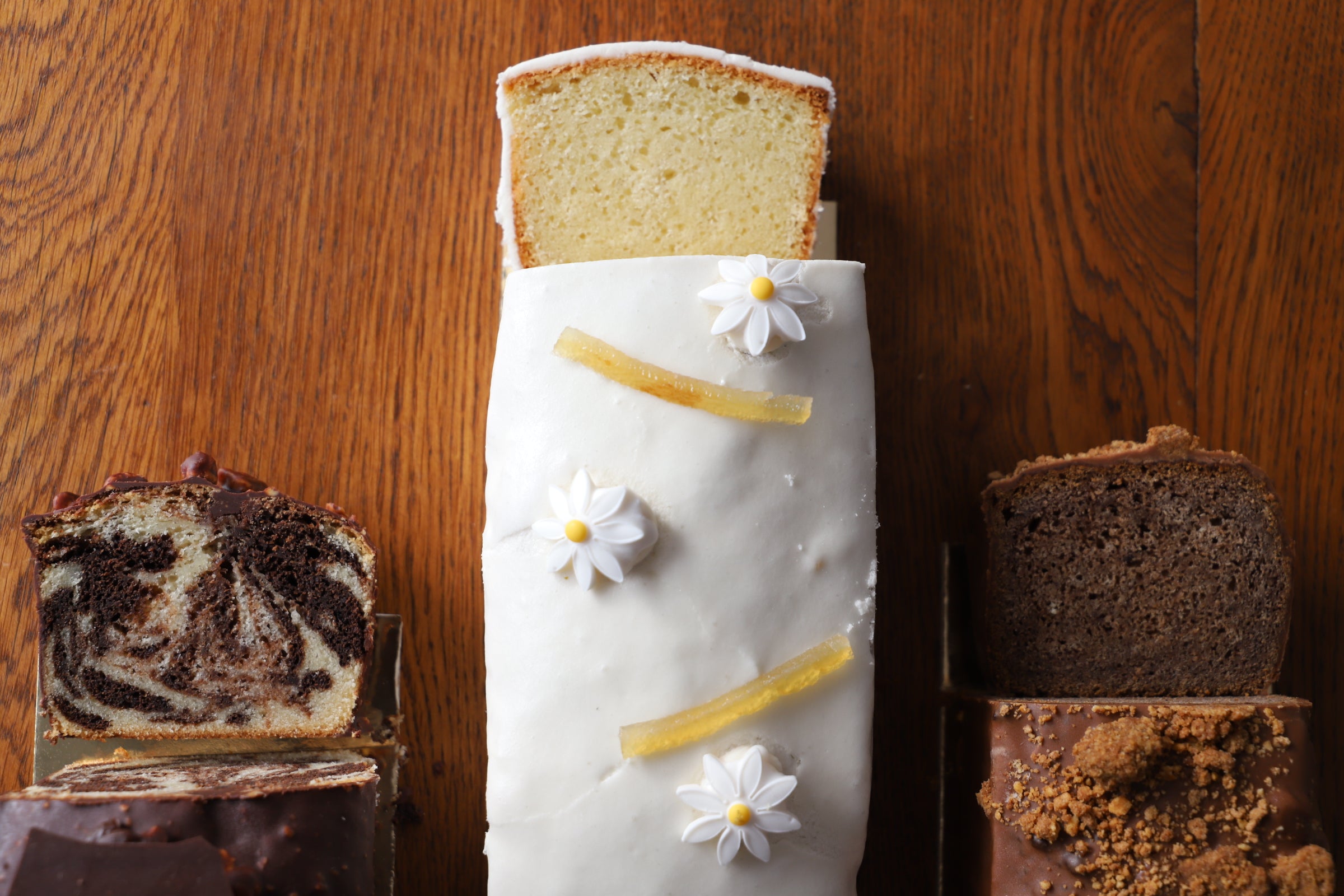 Lemon loaf with icing and decorative lemon zest next to a marble loaf and a plain loaf, beautifully displayed on a wooden table.